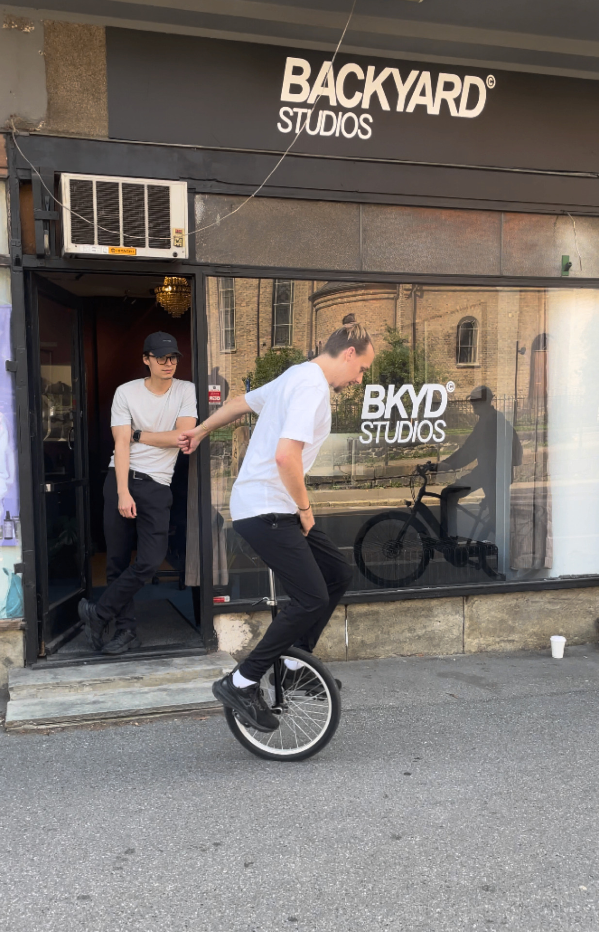 Kjartan og Turpal utenfor backyard studios i oslo. Kjartan syjkler på en enhjuls sykkel, Turpal i bakgrunnen