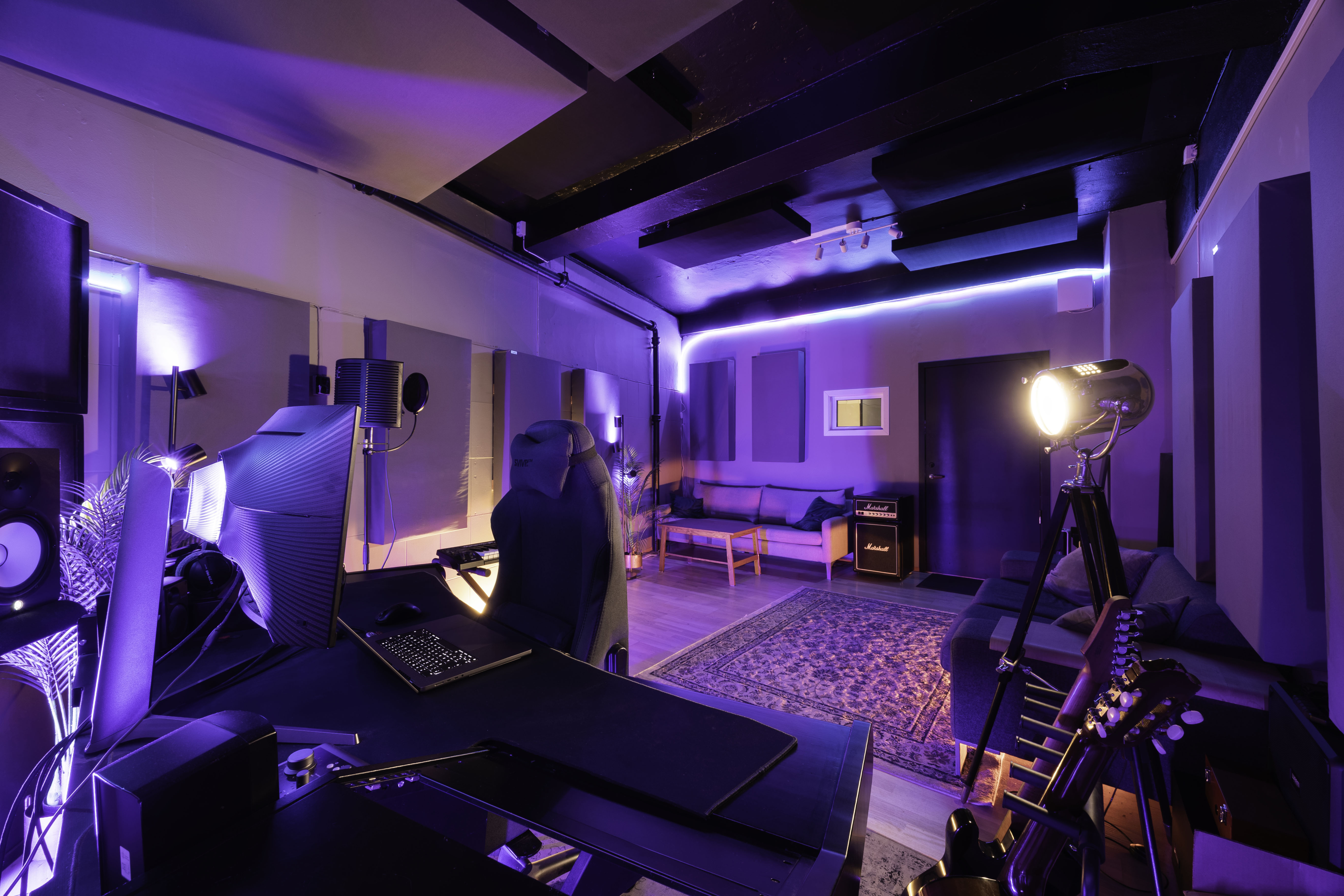 Bildet viser et kontrollrom for musikkinnspilling. Lilla lys fargelegger en pult med skjermer, instumenter og forsterkere langs med veggene.